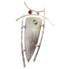 A fine Modernist gilt silver & multi-gemstone brooch. With a parcel-gilt central shield device framed by bamboo sides, a curved top, and bezel-set with stones. The gemstones include blue topaz, amethyst, and paste (or glass). Marked to the reverse with Joseph Downs / Sterling / 22. Simply a wonderful modernist brooch! Date: 21st Century Overall Condition: It is in overall good, as-pictured, used estate condition. There is some light edge wear, some fine and light surface scratches, and other signs of light wear consistent with age. Fineness: Marked Sterling for silver fineness. Marks: Marked to the reverse with Joseph Downs / Sterling / 22. Measurements: Height: ca. 110mm Width: ca. 67mm Depth: ca. 14mm Weight: ca. 29.5 g Items purchased from this dealer must delight you. Purchases may be Interesting Jewelry, Gemstone Brooch, Pin Ideas, Jewelry Styles, Top Ideas, Contemporary Jewelry, Modern Jewelry, Fine Silver, 21st Century