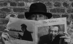 a man wearing a hat and holding up a newspaper with the image of two men on it