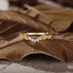 a gold ring with three diamonds on top of a leafy brown surface, in close up view