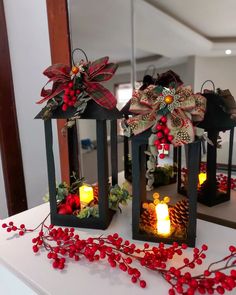 two lanterns with bows and candles are sitting on a white countertop next to red berries