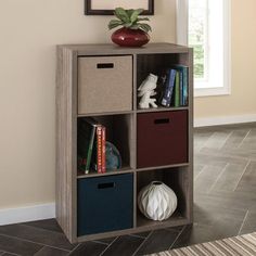 a book shelf with four bins and a vase on top