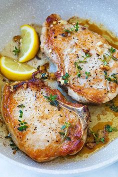 two pieces of meat in a bowl with lemon wedges