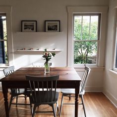 a dining room table with four chairs and a vase filled with flowers on top of it