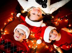 three children dressed up in christmas clothes and hats laying on the floor with their arms around each other