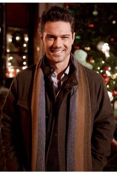 a man standing in front of a christmas tree with his hands in his pockets and smiling