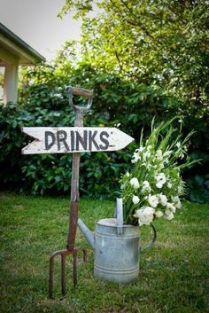 there is a sign that says drink with us on it and a watering can in the grass