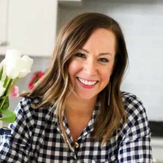 a woman holding a vase with flowers in it and smiling at the camera while sitting on a kitchen counter