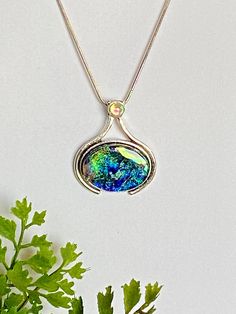 "❤Vibrant Dichroic Glass Pendant in a silver plated setting. This dichroic pendant is 34.6 mm X 30 mm (1.36 in  x .1.2 in).  The dichroic glass is set in a nickel free silver plated bezel with a 5 mm peridot Swarovski crystal at the top.   ❤It has been made with multiple layers of dichroic glass, hand shaped with a diamond saw, glass grinder and then fired multiple times in the kiln.  The pendant has a base layer of black and has vibrant dichroic colors of green, pink, blue and gold dichroic shimmers.  My glass designs are created with a passion for color, texture, and the dimensional dynamics that only multiple layers of glass create.   ❤Dichroic glass is produced by stacking layers of glass and micro layers of Quartz Crystal and Metal Oxides (which are vaporized in a vacuum chamber and t Iridescent Cabochon Necklace As Gift, Silver Glass Cabochon Necklaces, Silver Glass Cabochon Necklace, Silver Glass Necklace Keepsake, Silver Glass Necklace For Keepsake, Silver Glass Jewelry For Keepsake, Silver Necklace With Cabochon Glass, Silver Oval Pendant Jewelry Gift For Mom, Silver Oval Pendant Jewelry For Mom