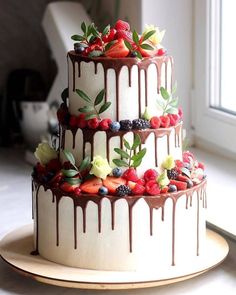 a three tiered cake decorated with fresh berries and chocolate drizzle