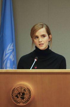 a woman standing at a podium with a microphone in front of her and an un flag behind her