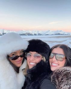 three women taking a selfie in front of the snow covered mountains at sunset with sunglasses on