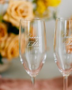 two champagne glasses with names on them sitting next to flowers and a vase in the background