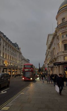 a red double decker bus driving down a street next to tall buildings