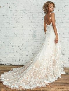 a woman standing in front of a white brick wall wearing a dress with flowers on it