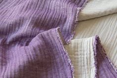 an old purple and white blanket is laying on top of each other, with holes in the fabric