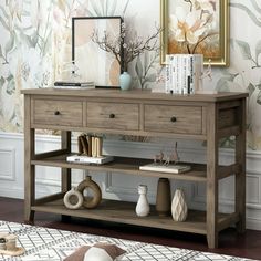 a wooden table with two drawers and some pictures on the wall behind it in front of a flowered wallpaper