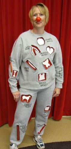 a person wearing a clown nose and grey sweat suit with hearts on the side, standing in front of a red curtain