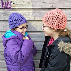 two young women standing next to each other near a wooden wall wearing knitted hats