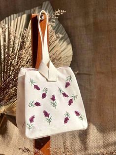 a white bag with purple flowers on it sitting next to a fan and dried grass