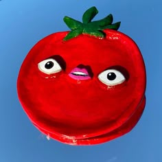 a close up of a red object with eyes and a tomato on it's head