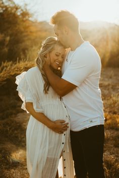 a pregnant couple cuddles in the desert at sunset during their family photo session