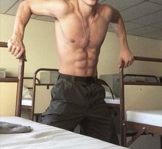 a shirtless man standing in front of a bed with his hands on his hips