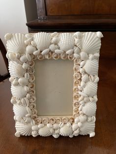 a frame made out of seashells on a table with a chair in the background