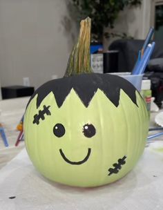 a pumpkin with a face painted on it sitting on a table next to markers and pens