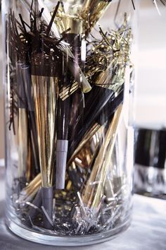 a glass jar filled with lots of gold and silver colored straws on top of a table