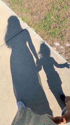 the shadow of a person standing next to a skateboard on a sidewalk with grass in the background