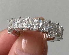 a hand holding a diamond ring in it's right hand, with the middle one being surrounded by smaller diamonds