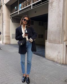 a woman standing in front of a building while looking at her cell phone and wearing black shoes