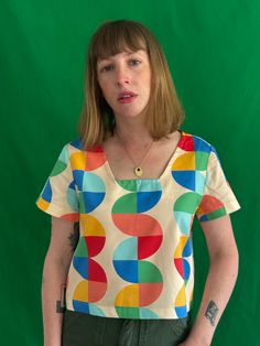 Crop top featuring a square neckline, short sleeves, loose fit, and mid-length. Its loose fit makes it ideal for layering to be worn year-round. Its bright bold print makes it a go-to statement piece. Hand-sewn with a linen cotton mix and made to order. White Short Sleeve Tops With Colorful Pattern, Multicolor Scoop Neck Tops For Summer, Green Retro Print Short Sleeve Tops, Green Short Sleeve Tops With Retro Print, Retro Short Sleeve Top With Vibrant Print, Multicolor Bold Print Short Sleeve Tops, Multicolor Print Bold Short Sleeve Tops, Green Geometric Pattern Tops For Summer, Bold Summer Tops With Abstract Print