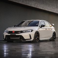 a white car is parked in front of a garage door with black rims on it