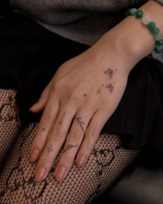 a woman's hand with a tattoo on her left wrist and green beaded bracelet