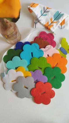 colorful felt flowers are on a plate next to a vase