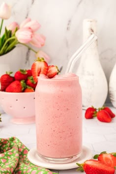 a pink smoothie with strawberries on the side and flowers in vases behind it