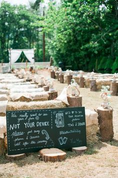 a chalkboard sign sitting on top of a pile of hay next to wooden stumps