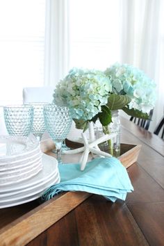 a wooden table topped with plates and vases filled with flowers on top of it