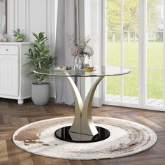 a round glass table sitting on top of a wooden floor next to a potted plant