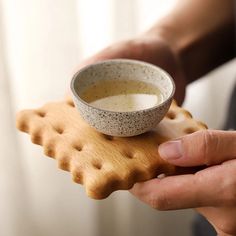 a person holding a plate with a bowl on it and some crackers in front of them