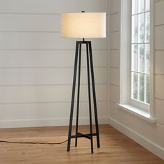 a floor lamp with a white shade on it in front of a window and wood floor