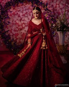 a woman in a red wedding gown and veil with flowers on the wall behind her