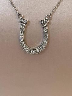 This stunning Diamond Horseshoe Necklace features a gorgeous 18k white gold horseshoe pendant sparkling with 25 pave-set round brilliant cut diamonds. The horseshoe is a universal symbol of good luck, making this necklace a perfect way to add a touch of elegance and fortune to any outfit. The pendant hangs from a dainty 18-inch chain, also crafted from 18k white gold. Although the origins are not exactly known, it is believed that the horseshoe became the symbol of luck when the eighth century C Luxury Horseshoe Jewelry For Formal Occasions, Luxury Horseshoe-shaped Formal Jewelry, White Gold Horseshoe Jewelry For Anniversary, Elegant Horseshoe Jewelry For Anniversary, Elegant Silver Horseshoe Necklace, Formal Horseshoe Jewelry With Diamond Accents, Formal Horseshoe Diamond Jewelry, Elegant Sterling Silver Horseshoe Jewelry, Classic Horseshoe Jewelry With Diamond Accents