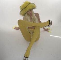 a woman sitting on the ground wearing yellow tights and a furry hat with her legs spread out