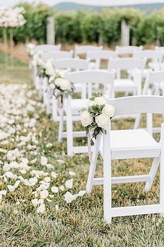 rows of white chairs with flowers on them in an outdoor ceremony area at a winery