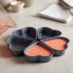 four heart shaped pans with sauce in them on a table next to a pitcher