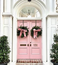 two wreaths are on the front door of a house with pink doors and windows