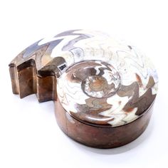 an old metal object with white and brown designs on it's sides, sitting on a white surface