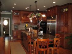 a large kitchen with wooden cabinets and an island in the center is lit by three pendant lights